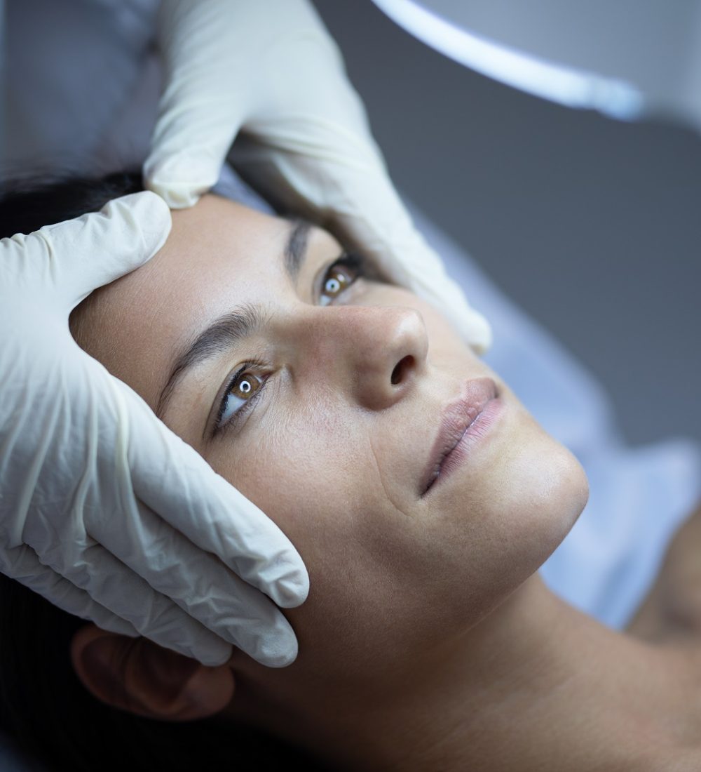 Side view of a female surgeon examining her Caucasian patient during plastic surgery in clinic